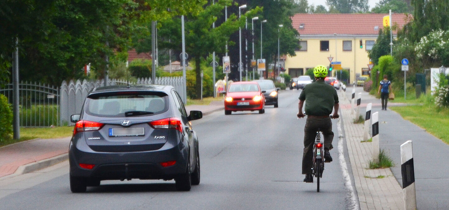 Ein Auto überholt einen Radfahrer und hält sich dabei weit entfernd von ihm