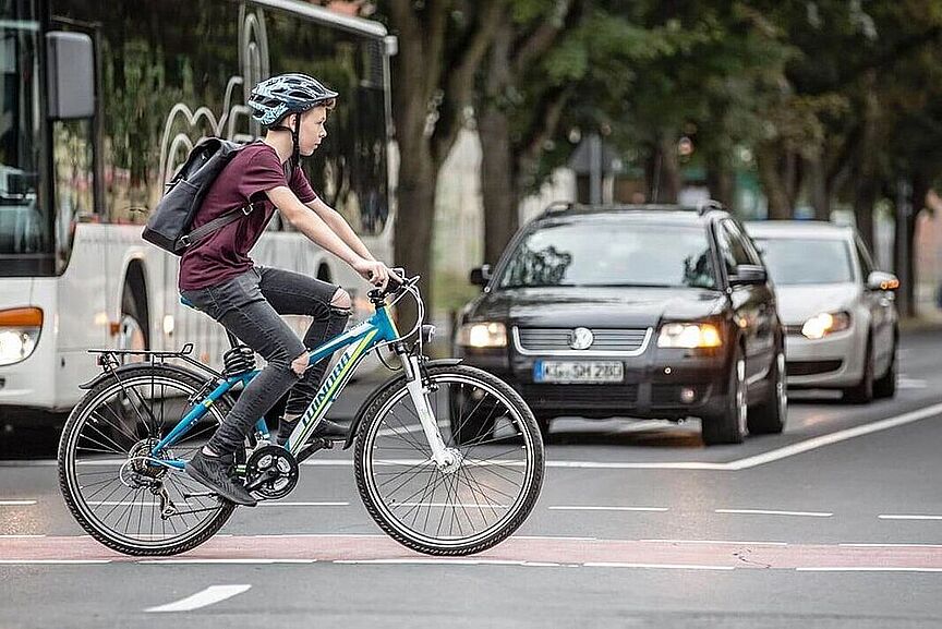 Sicherer Schulweg? Junge fährt auf dem Fahrrad über einen rot markierten Radweg an wartenden Autos vorbei.