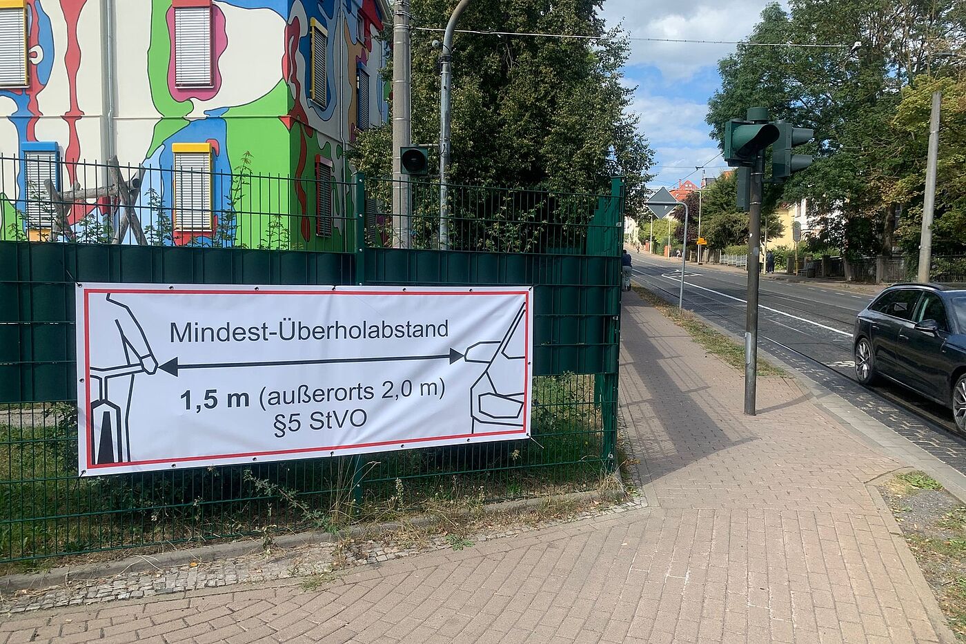 Ein Banner an einem Zaun macht auf den beim Überholen von Radfahrenden einzuhaltenden Mindestabstand aufmerksam.