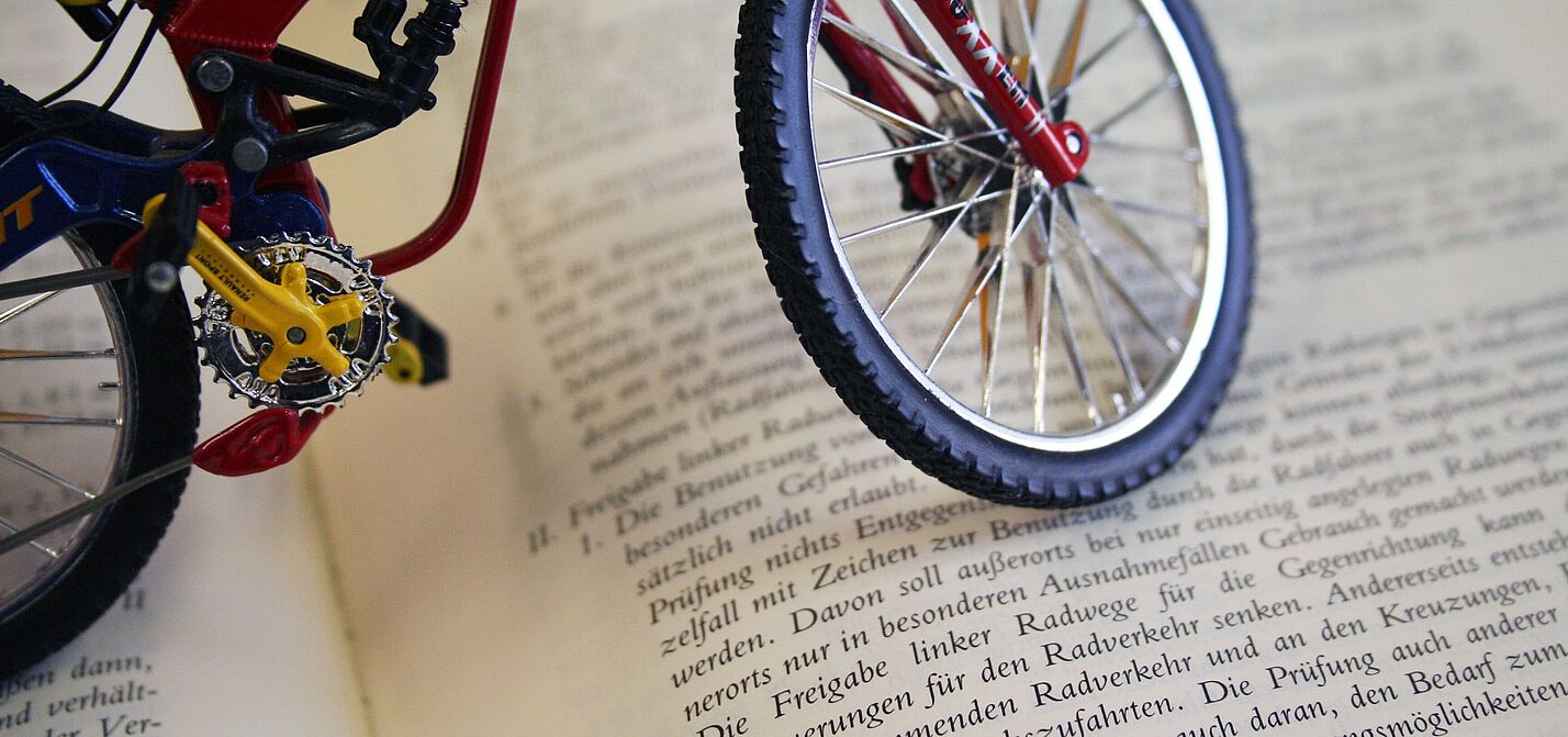 Miniatur-Fahrrad steht auf einem aufgeschlagenen Buch mit deutschem Gesetzestext.