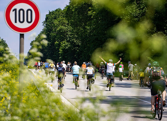 Radfahrer bei Sternfahrt neben Schild zu Geschwindigkeitsbegrenzung 100h/km